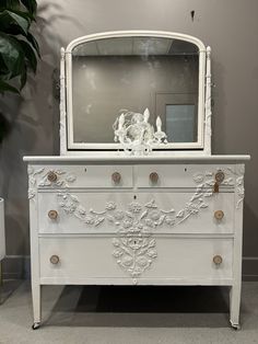 a white dresser with a mirror on top of it next to a potted plant