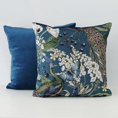 two blue pillows sitting next to each other on a white table with flowers and peacocks