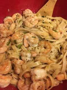 pasta with shrimp and pesto in a red bowl next to a wooden spatula