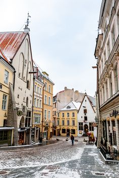 people are walking down the street in an old town with snow on the ground and cobblestone streets