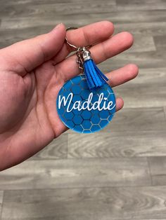 a hand holding a blue keychain with the word naddie on it