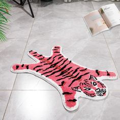 a pink tiger rug sitting on top of a white tile floor next to a book