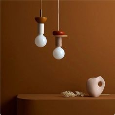 three light bulbs hanging from the ceiling above a table with a vase and other items on it