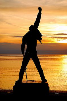 the silhouette of a person standing in front of a body of water with their arms up