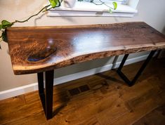 a wooden table with metal legs and a plant on it in front of a window