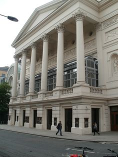 a large white building with columns and people walking on the sidewalk in front of it