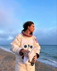 a man standing on top of a sandy beach next to the ocean wearing an astronaut suit