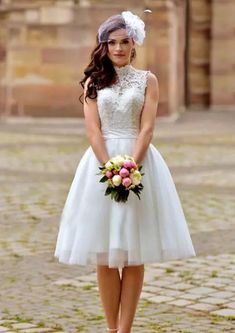 a woman in a white dress standing on a cobblestone street with her hands behind her back