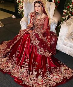 a woman in a red and gold wedding dress sitting on a white chair