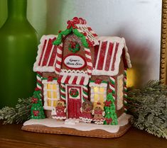 a gingerbread house decorated for christmas on a table next to a green vase with greenery