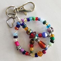 "Groovy gift for that free spirited friend or relative! Each bright and colorful Beaded Wire Peace Sign Keychain is an original, unique and one of a kind. Made from sturdy, tarnish resistant wire, using only quality beads and adorned with a .25\" alloy steel heart charm. Swivel base and lobster claw opening for easy clip on and off. Because no two are alike your item will differ from what is pictured." Word Keychain Beads, Easy Bead Crafts For Adults, Gifts For Hippie Friends, Glass Bead Keychain Diy, Keychain Ideas Diy Beads, Beaded Gifts Diy, Diy Beaded Charms, Brad Keychain, Cute Things To Make With Beads