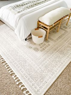 a white bed sitting on top of a rug next to a wooden chair and ottoman