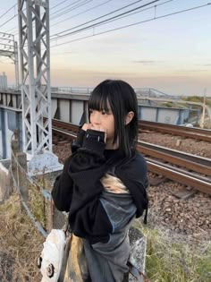 a woman standing on the side of a train track while talking on a cell phone