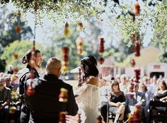 a man and woman standing in front of an audience at a wedding ceremony with confetti hanging from the trees