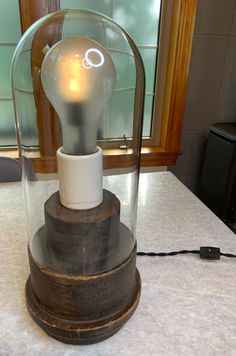 a light bulb in a glass case on top of a marble counter with a window behind it