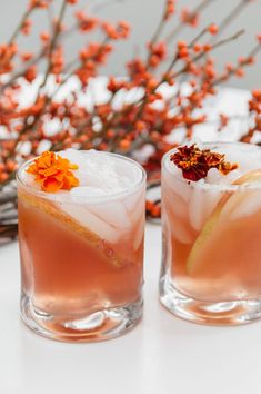 two glasses filled with drinks sitting on top of a white table next to orange flowers