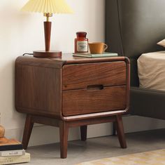 a night stand with a lamp on top of it next to a bed and nightstand