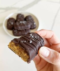 a hand holding a half eaten chocolate covered cookie in front of a plate of cookies