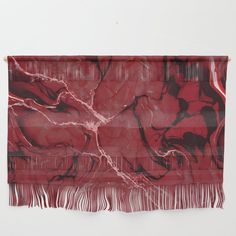 a red and black wall hanging with fringes on it's sides, in front of a white wall