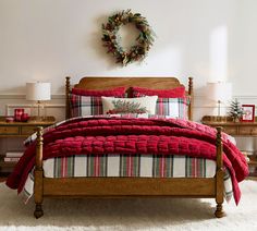 a bed with red blankets and plaid comforter in a white bedroom decorated for christmas