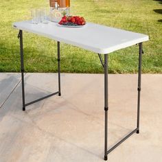 a table with drinks and fruit on it in the middle of a lawn area next to a fence