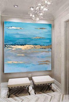 a large painting hanging on the wall in a room with two stools and a chandelier