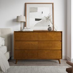 a bedroom scene with focus on the chest of drawers and a large framed art piece