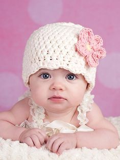 a baby girl wearing a crocheted hat on top of a white blanket in front of a pink background