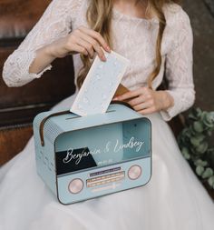 a woman in a white dress is holding a blue box with a card on it