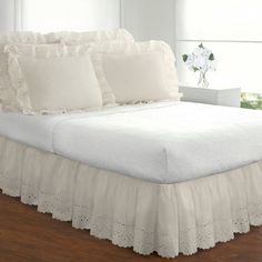 a bed with white ruffled bedspread and pillows