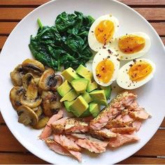 a white plate topped with meat, vegetables and hard boiled eggs