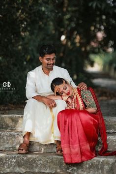 a man sitting next to a woman on top of a stone step in front of trees