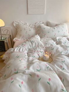 a white bed with pink flowers on it and a small candle in the middle of the bed