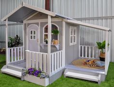 a doll house is set up on the grass in front of a building with white sidings