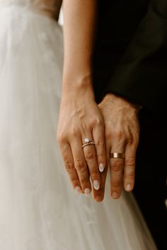 the bride and groom are holding hands with their wedding rings on their fingers as they stand close to each other