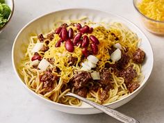 a white bowl filled with spaghetti and meat covered in cheese, onions and chili sauce