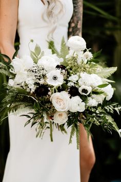 a bride holding a bouquet of white and black flowers with greenery in the background