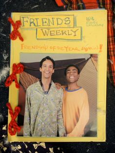 a couple of men standing next to each other in front of a yellow sign that says friends weekly