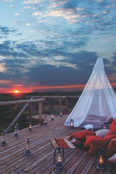 an outdoor deck with candles and pillows on it at sunset or dusk, overlooking the ocean