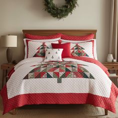 a red and white quilted bed with christmas decorations on the headboard, along with a wreath