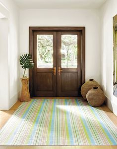 an entryway with a striped rug, potted plant and wooden front door on the side