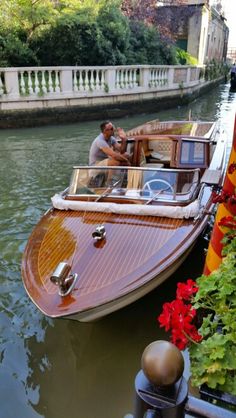 a man driving a boat down a river next to a bridge with flowers growing on it