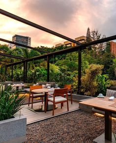 an outdoor dining area with wooden tables and chairs, surrounded by greenery at sunset