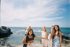 four girls standing on the beach with their arms around each other and one holding a sign