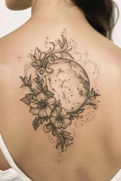 the back of a woman's shoulder with flowers and a moon tattoo on it