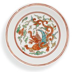 a white plate with an orange and blue dragon design on the front, sitting on a white surface