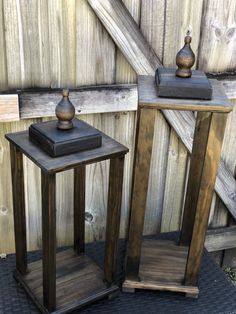 two wooden tables sitting next to each other on top of a black tile floor in front of a wooden fence