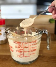 a hand holding a spoon over a measuring cup filled with batter