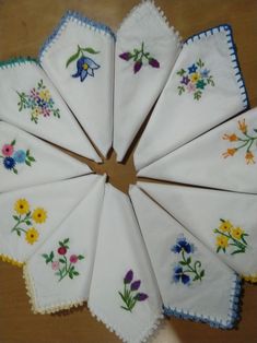 six embroidered napkins arranged in a circle on top of a wooden table with flowers