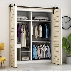 an open closet with clothes hanging on the doors and a clock in the corner next to it